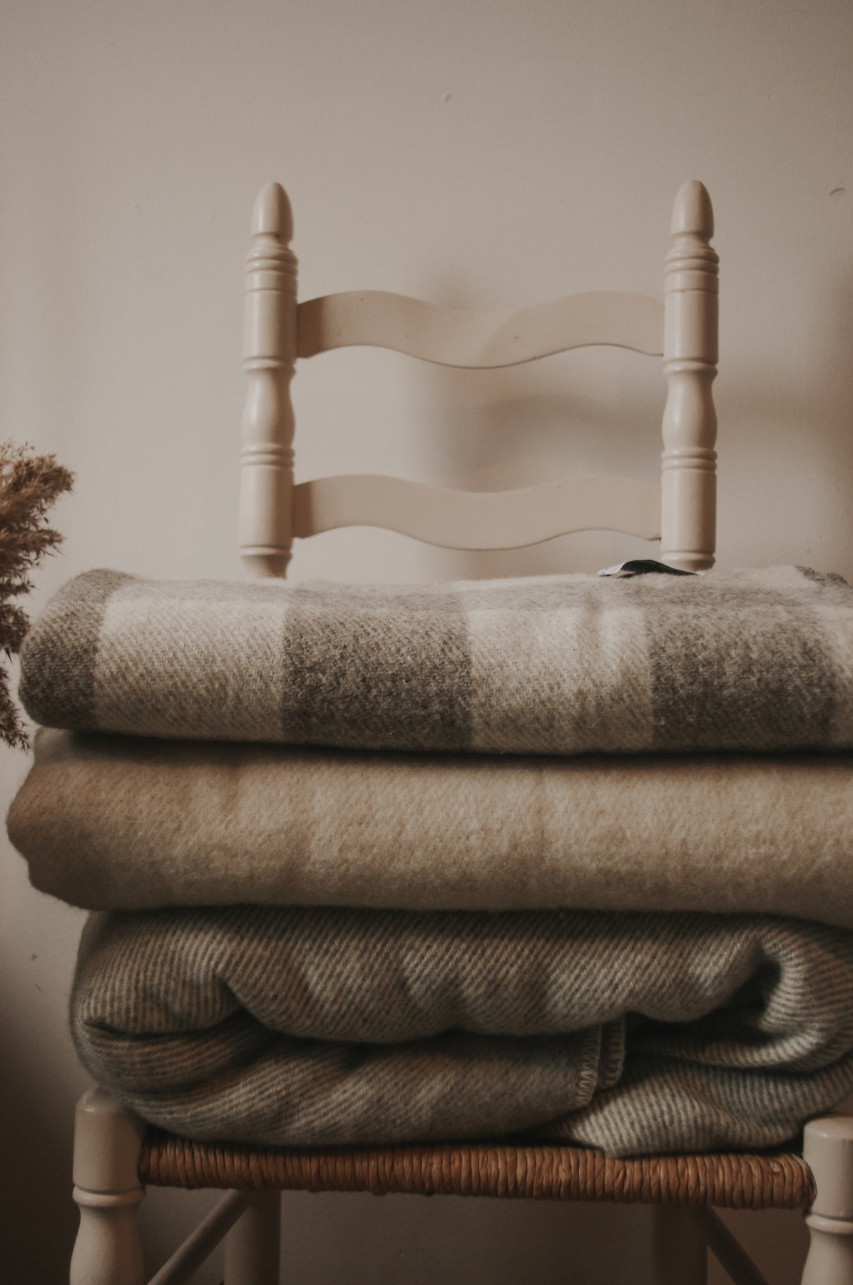 Topsy Farms' wool blankets in natural white and grey, folded on a white wooden chair