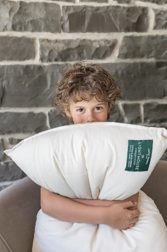 curly-haired child grinning and clutching Topsy Farms' Lighthouse Collection wool filled pillow, in front of a stone wall