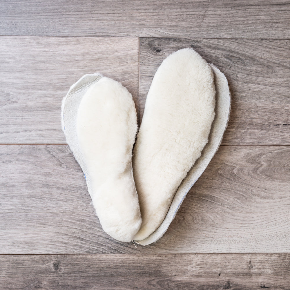 Two pairs of fluffy white sheepskin insoles on a barn board background
