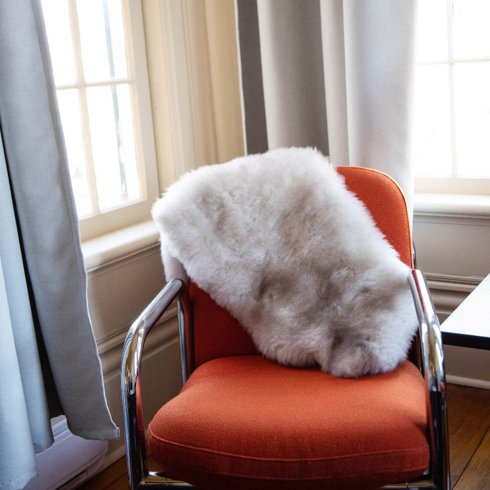 Topsy Farms' naturally coloured lambskin draped over an orange fabric chair in a sunny corner