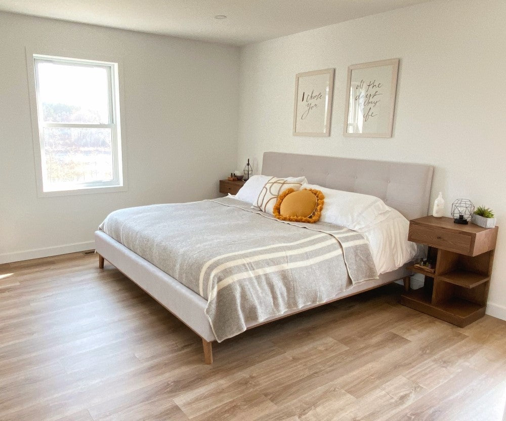 Topsy Farms' light grey tweed blanket on a king bed with fabric headboard, in a minimalist room with white walls and pale wood floor