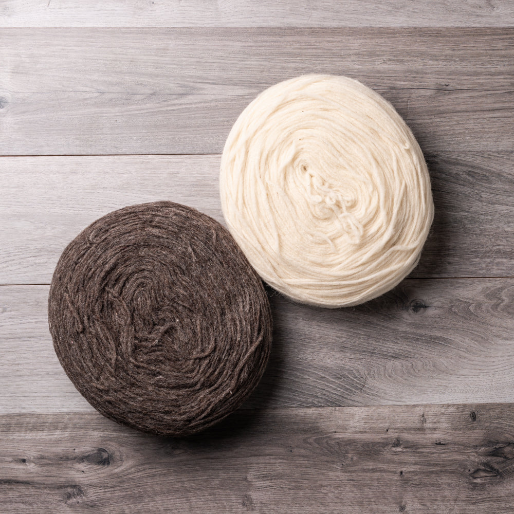 One white and one brown circular bundles of spun wool, on a barn board background