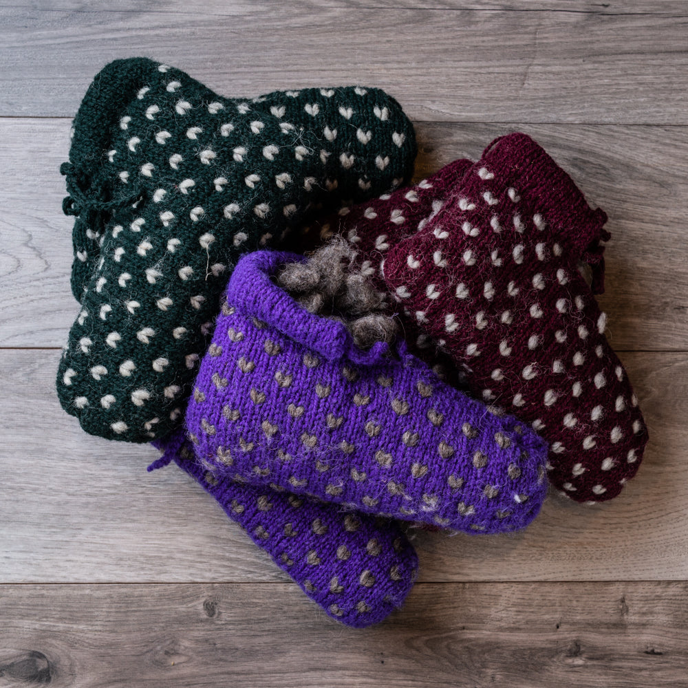 Dark green, purple, and burgundy knitted ankle-book style slippers with white accent Vs throughout, on barnboard