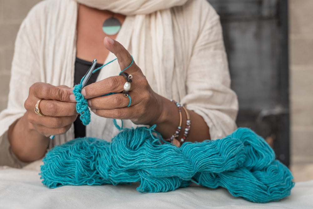 brown woman crocheting Topsy Farms' turquoise yarn