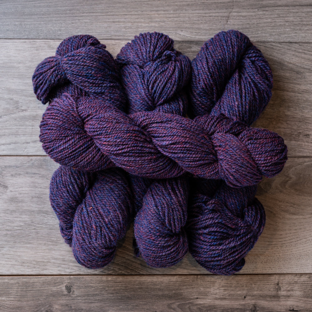 4 skeins of purple heather yarn on a barn board background