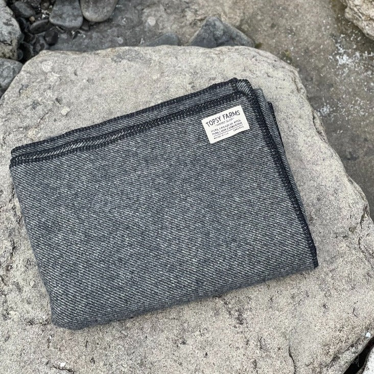 Topsy Farms' charcoal tweed wool throw blanket on limestone rocks