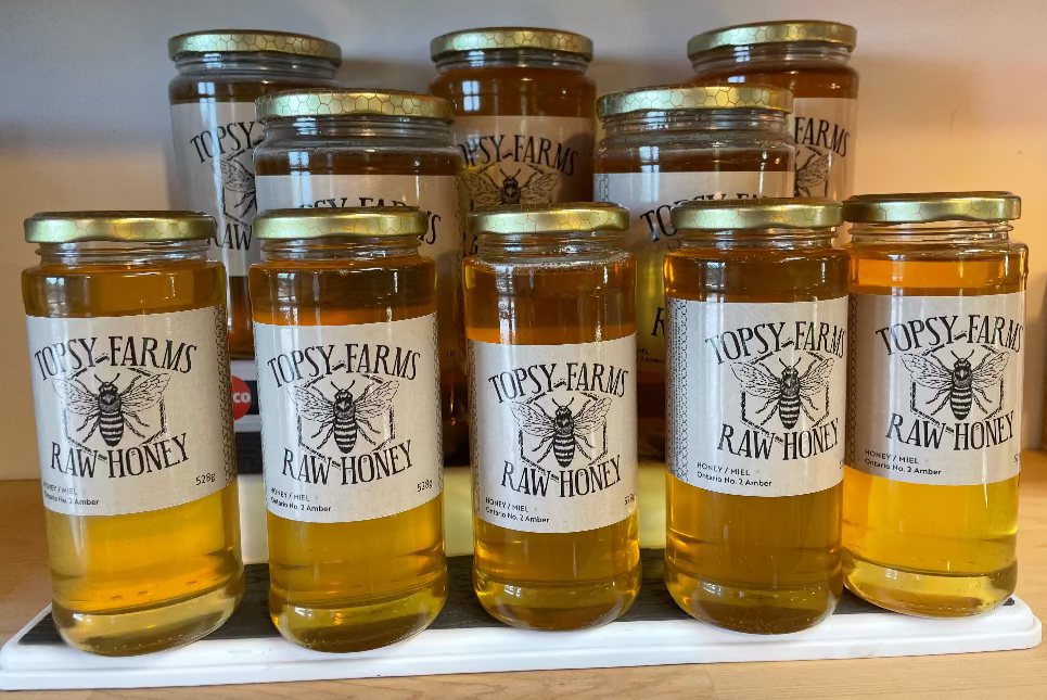 Jars of Topsy Farms Raw Honey on a wooden surface