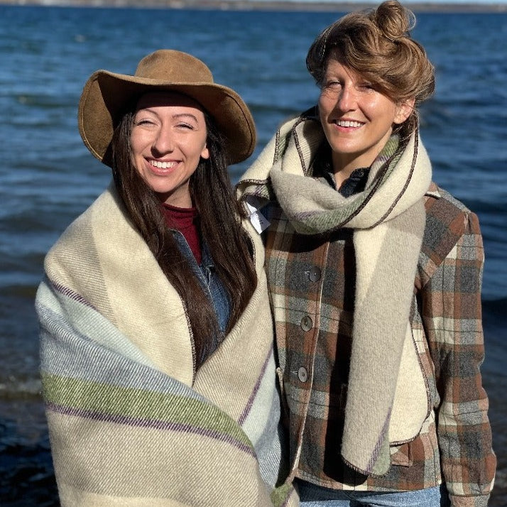Two women standing by a lake, wearing Topsy Farms' Shoreline wrap and scarf