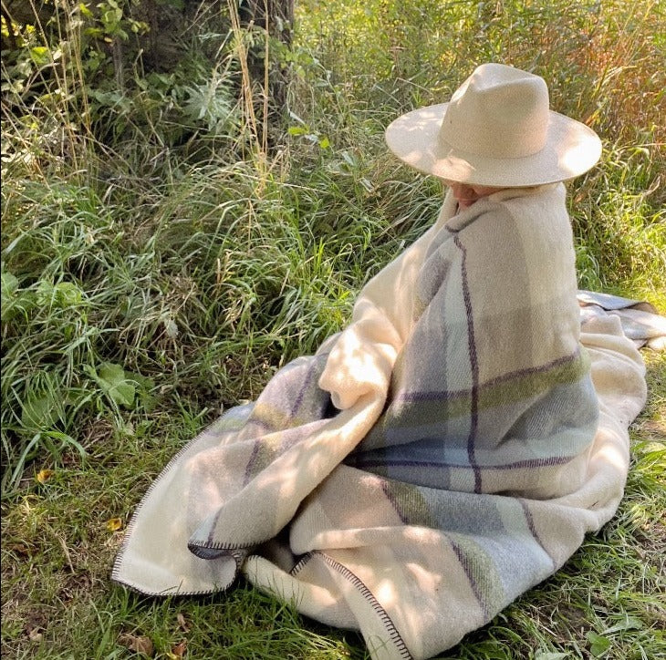 Person in straw hat in a field wrapped in Topsy Farms' unique Shoreline wool blanket