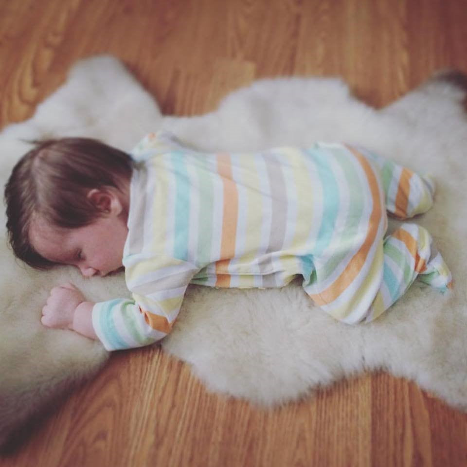 Dark-haired baby in striped onsie, sleeping face down on a white lambskin