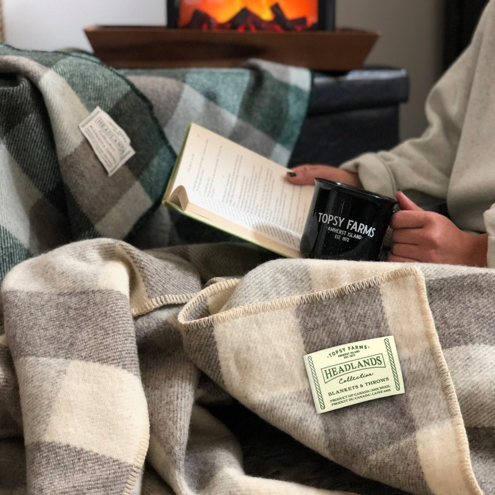 Woman reading by a fireplace, with Topsy Farms' grey and white and grey and green checkerboard wool blankets