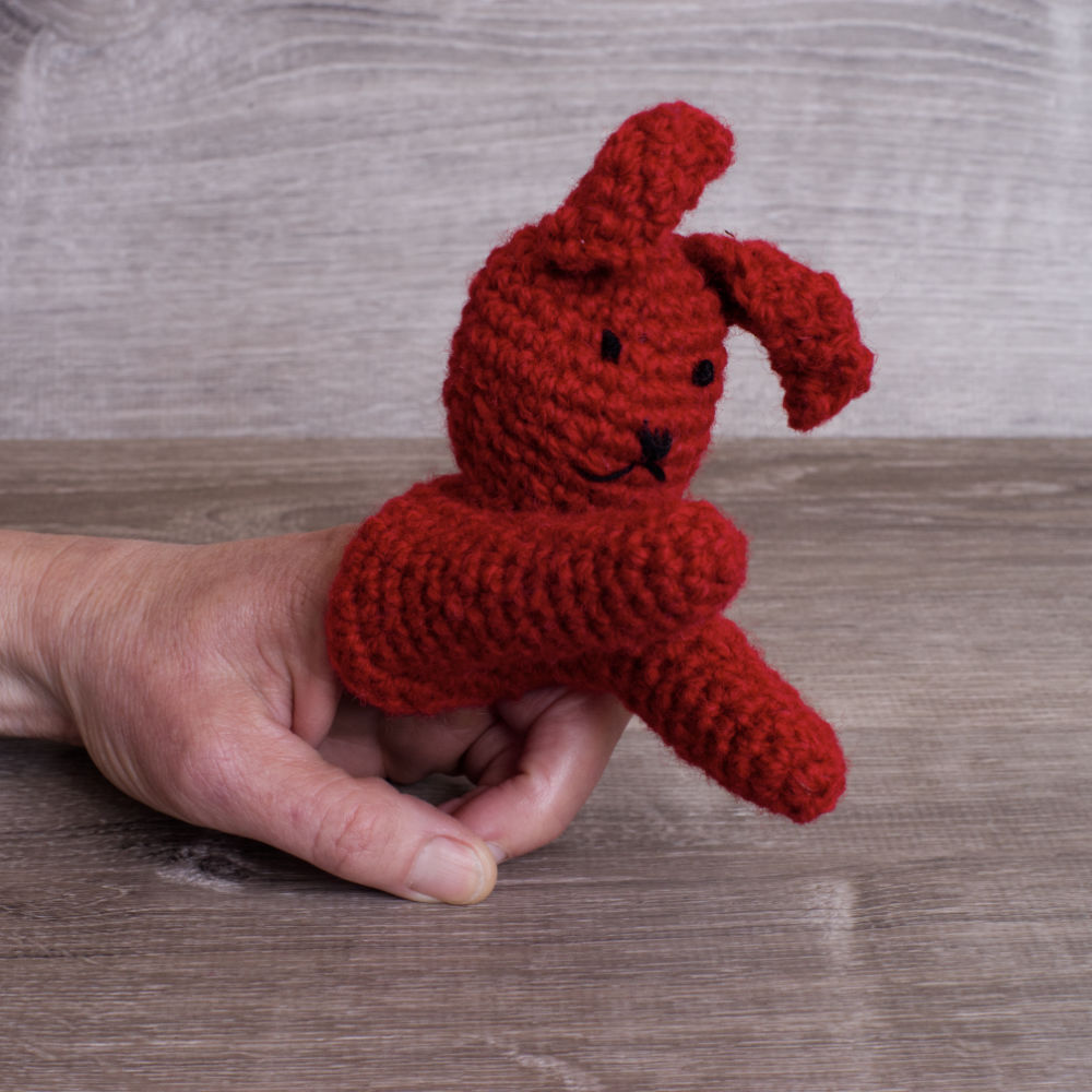 Red knitted wool bunny finger puppet on a white hand
