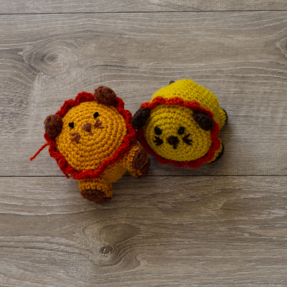 Two handmade wool lions, one yellow, one orange, on a grey barn board background