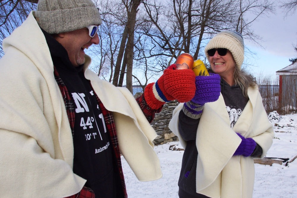 Couple standing in the snow, cheersing MacKinnon beers with Topsy Farms' wool beer mitten