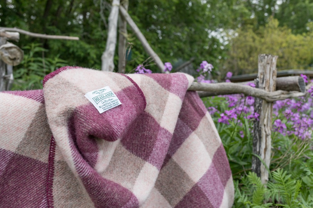 Topsy Farms' burgundy and pink checkerboard wool blanket, draped over a wooden fence in a garden