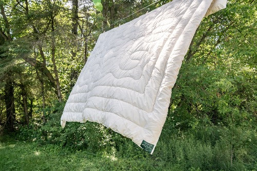 Topsy Farms' Lighthouse collection wool filled duvet hanging on a clothesline with trees in the background