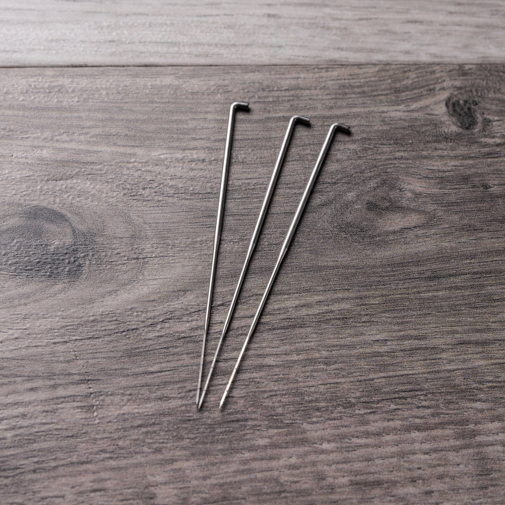 3 long, tapered metal needles with a slight hook at the top on a barn board background