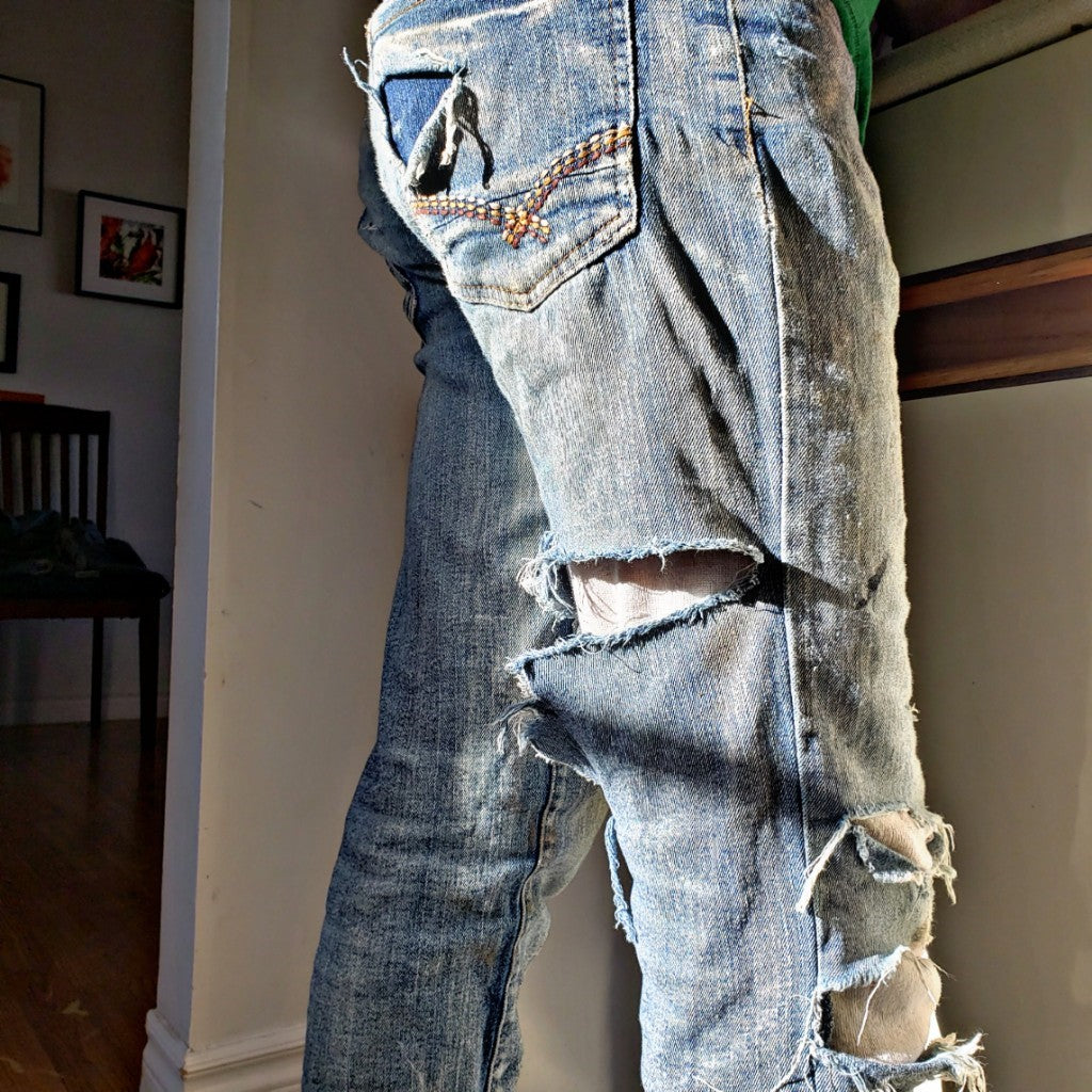 Pair of ripped, faded jeans pictured from the waist down, in a sunny living room