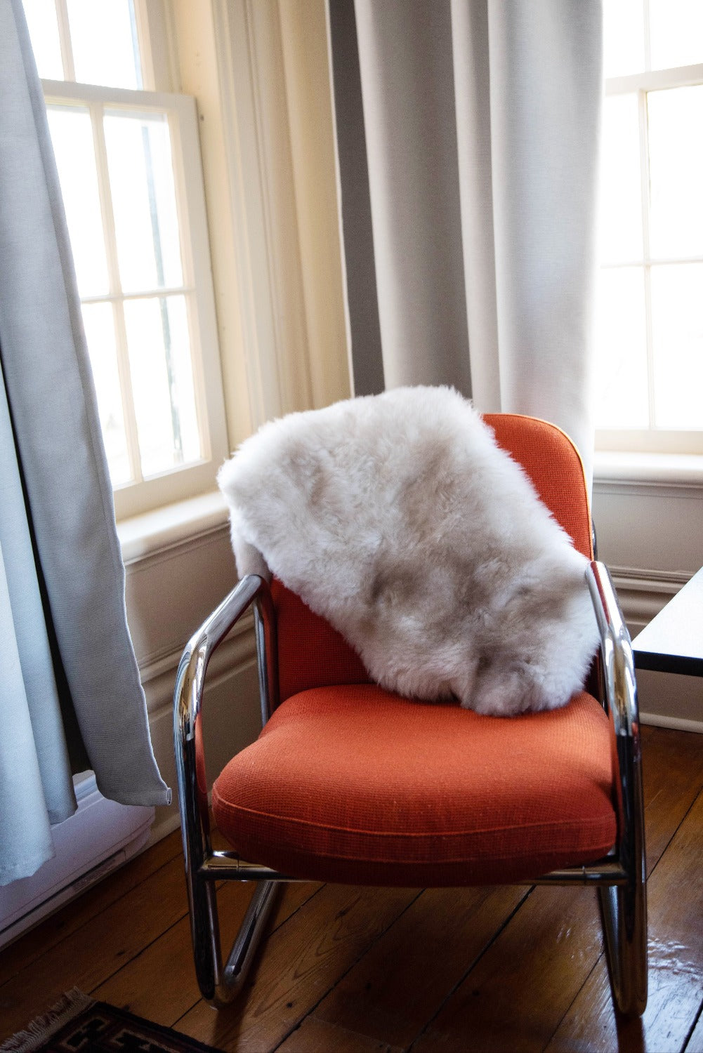 Topsy Farms' naturally coloured lambskin draped over an orange fabric chair in a sunny corner