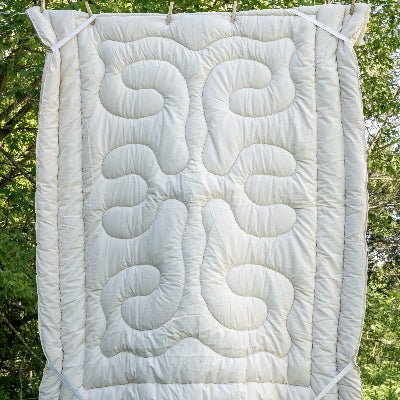 Topsy Farms' wool filled mattress topper hanging on a clothesline with trees in the background