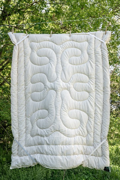 Topsy Farms' wool filled mattress topper hanging on a clothesline with trees in the background