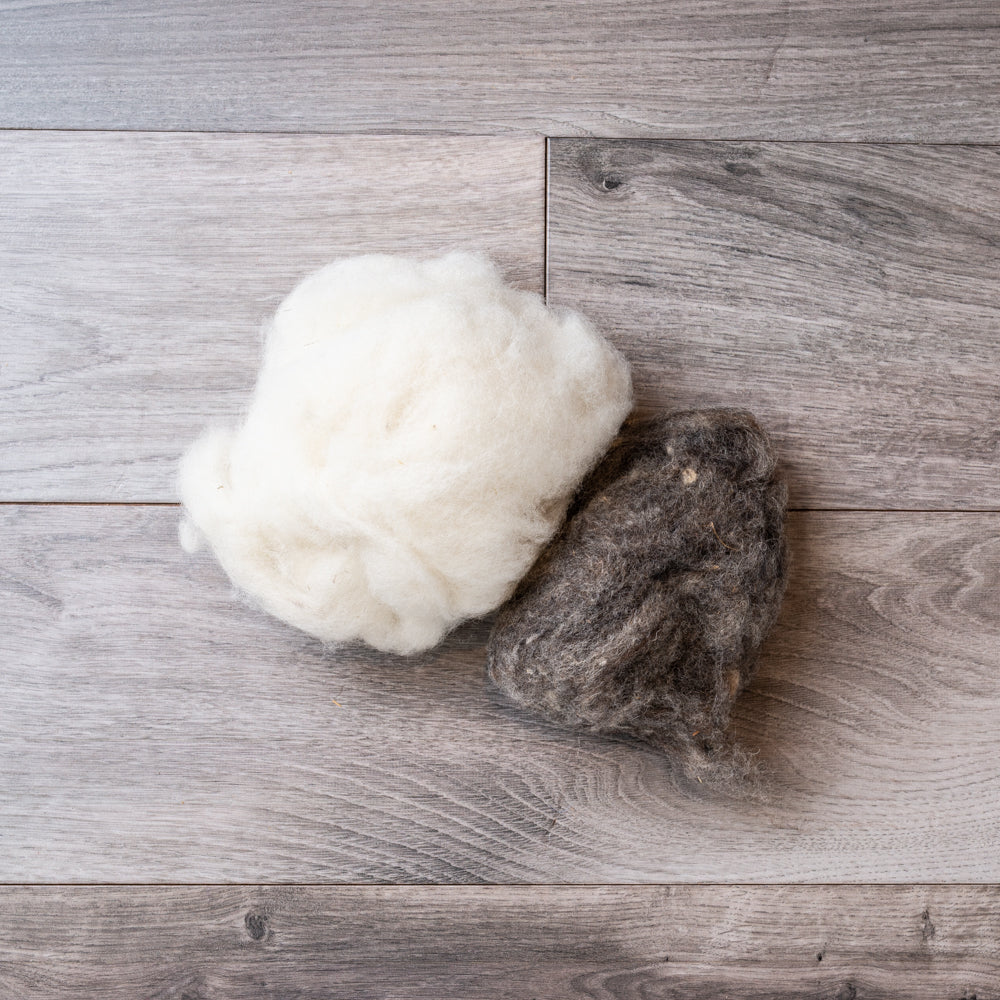 Two balls of unspun wool, one white and one dark grey, on a barnboard background