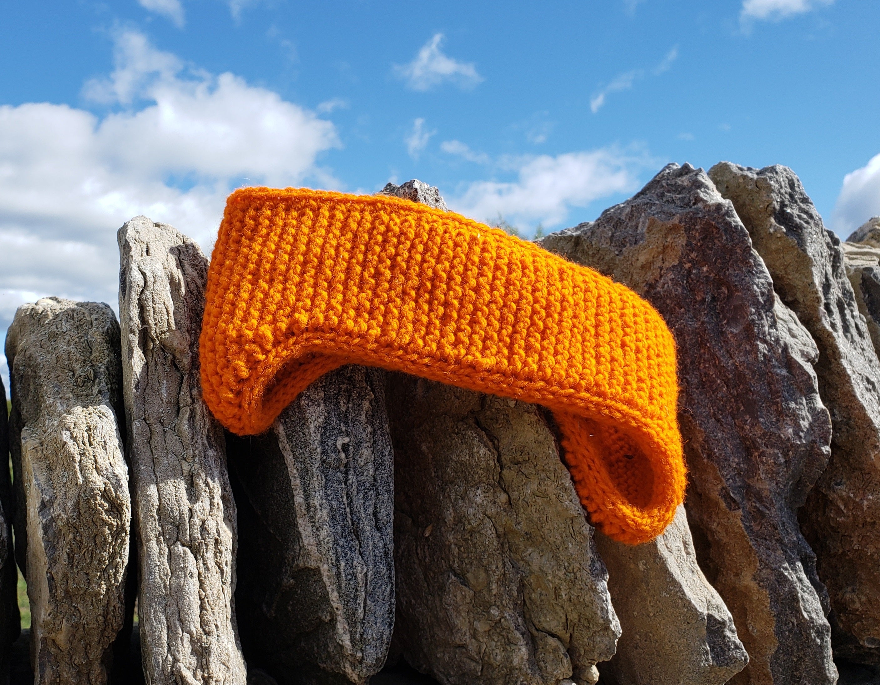 Topsy Farms' hand knit wool headband, in bright orange, on a stone wall