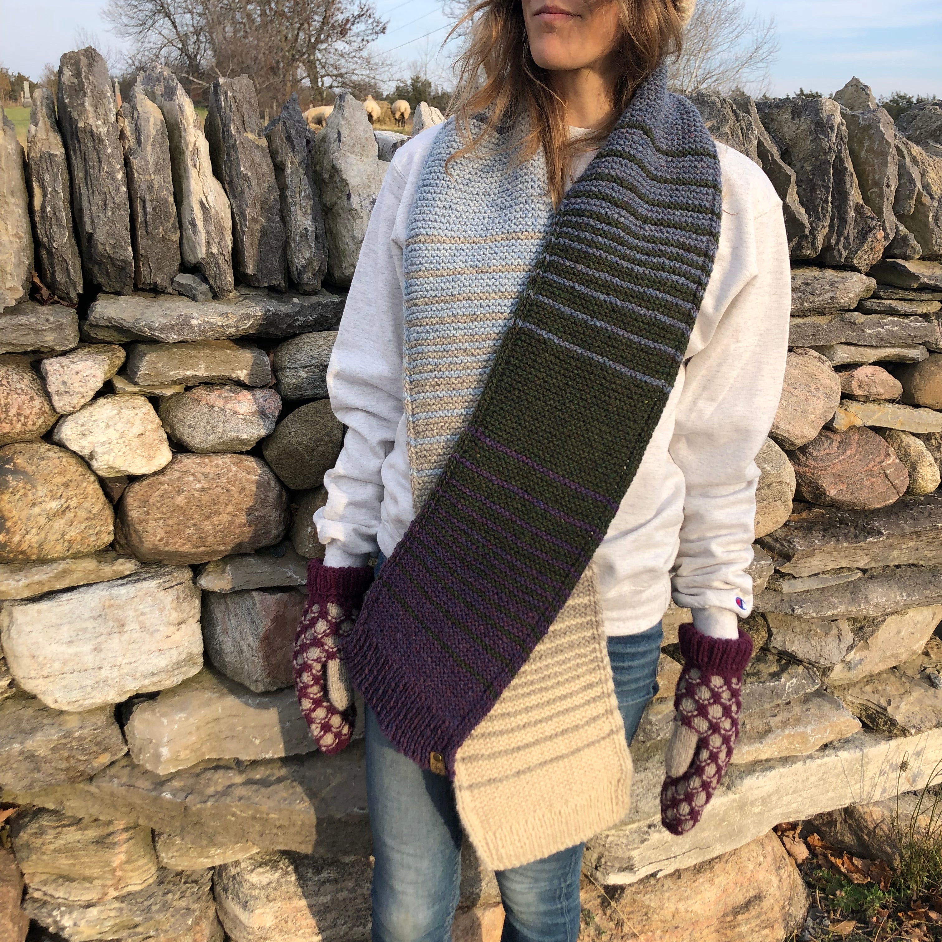 Blonde woman in front of a stone wall in Topsy Farms' Shoreline hand knit scarf and hat