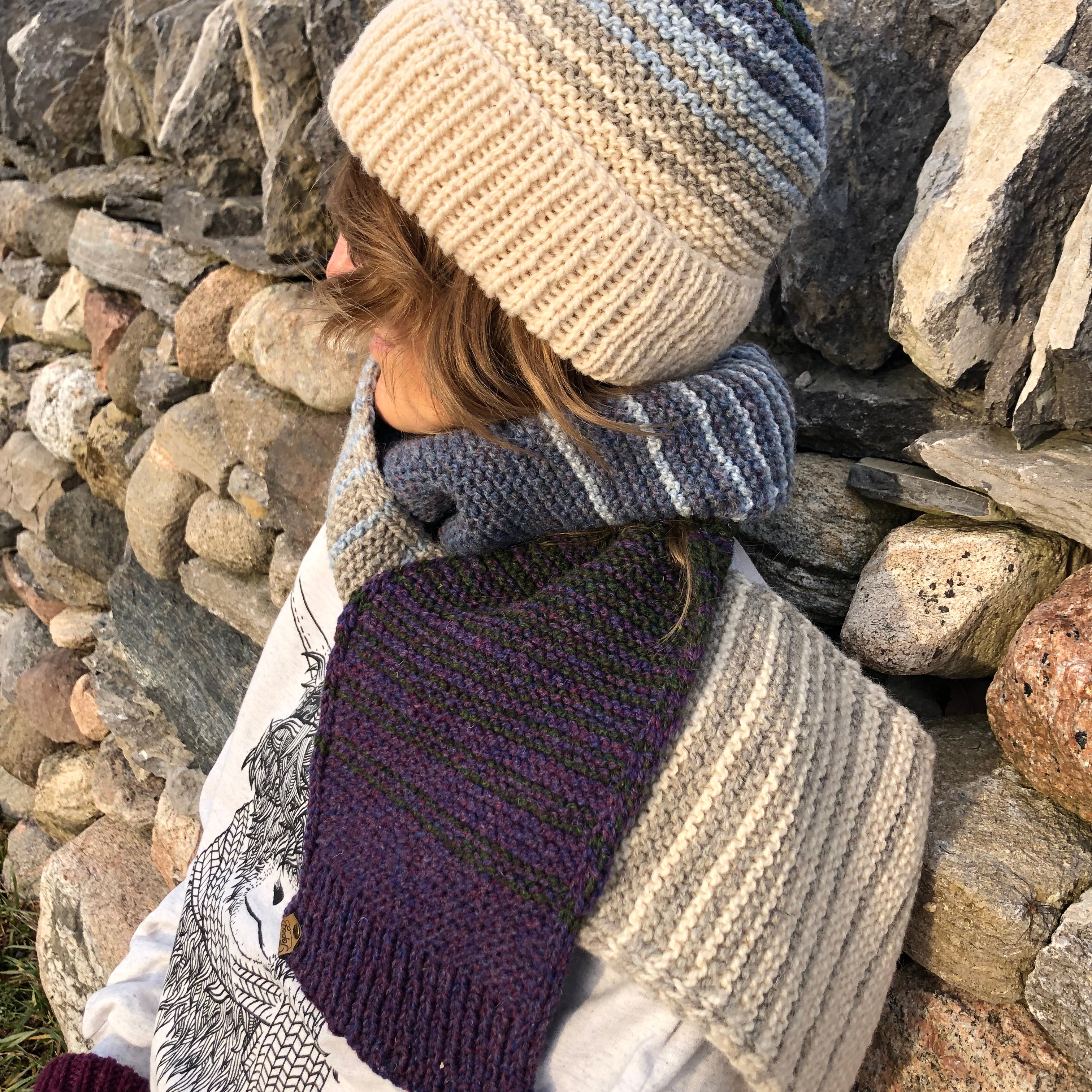 Blonde woman in front of a stone wall in Topsy Farms' Shoreline hand knit scarf and hat