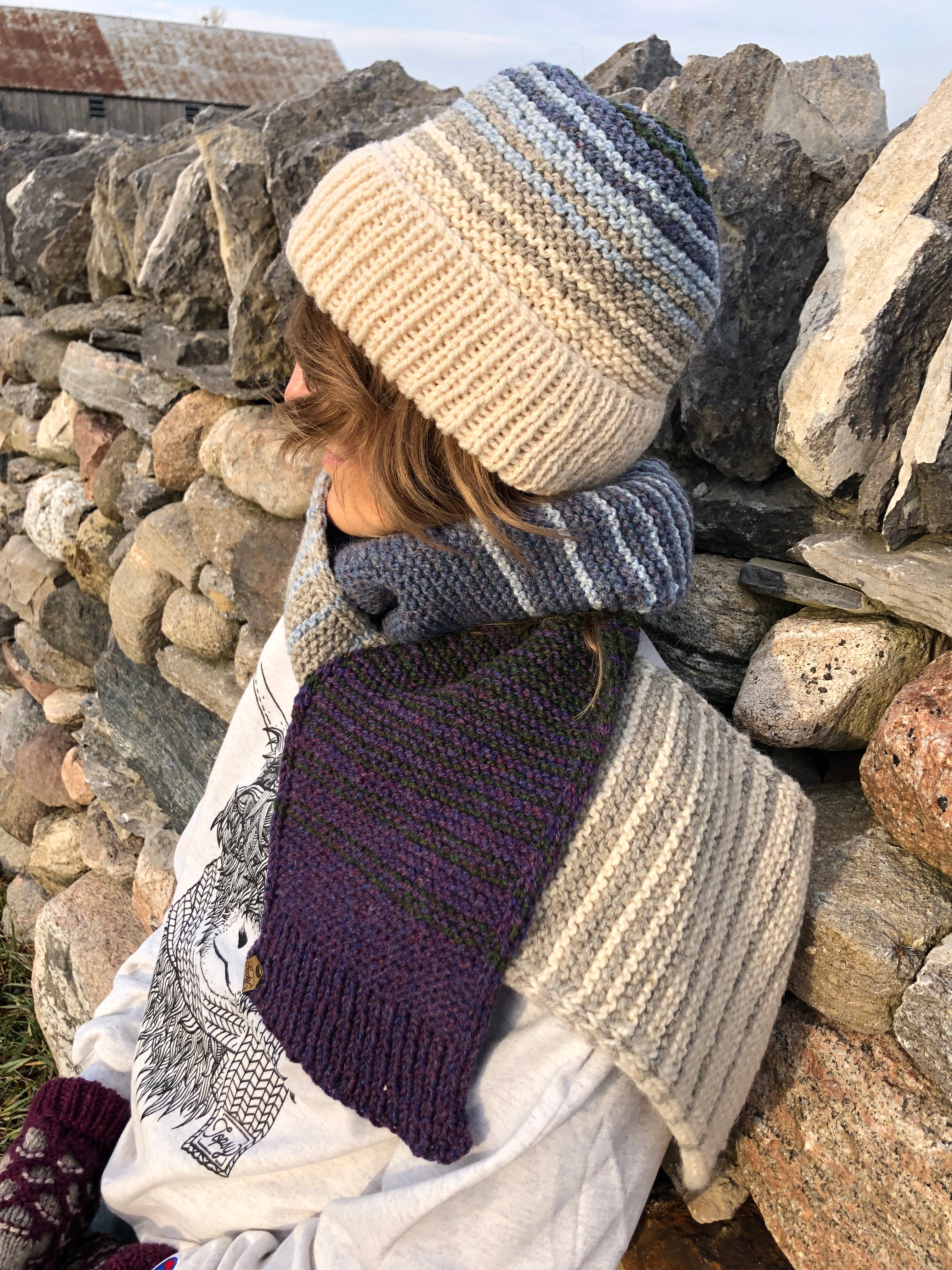 Blonde woman in front of a stone wall in Topsy Farms' Shoreline hand knit scarf and hat