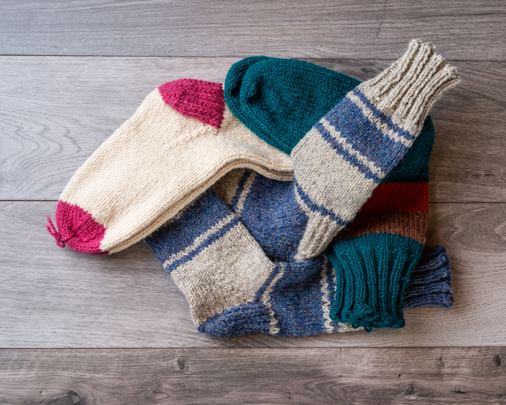 Knitted wool socks in a variety of colours, with stripes and contrasting heels and toes on barnboard backgroun