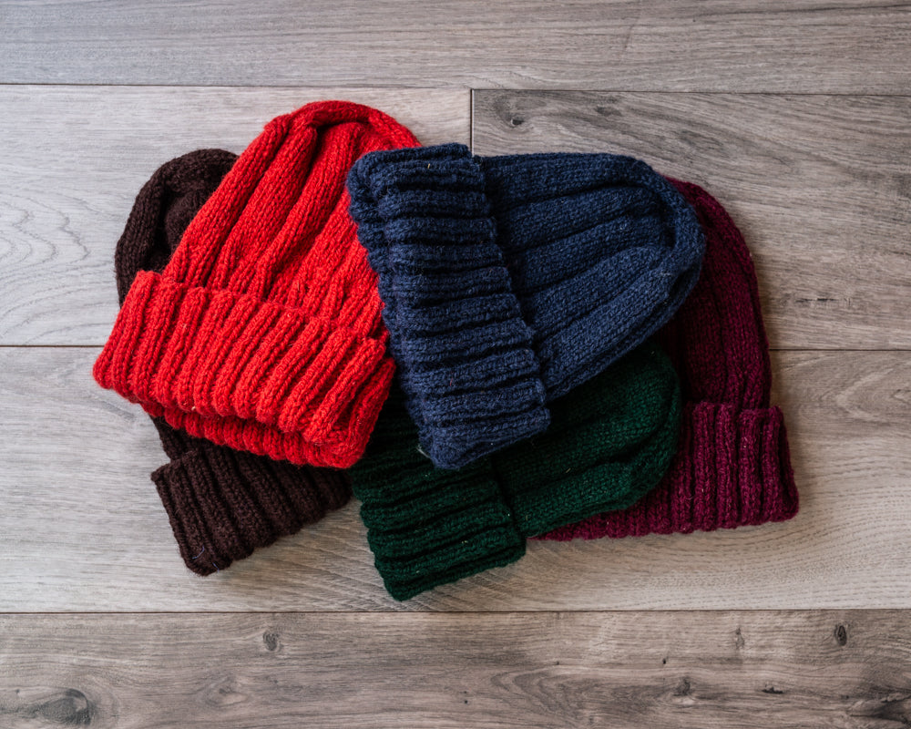 Red, navy blue, dark green, and burgundy knitted watch caps with brim folded up on barnboard